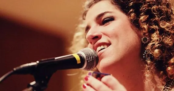 Fotografia em plano fechado da cantora Giana Viscardi cantando em um microfone durante uma apresentação ao vivo.