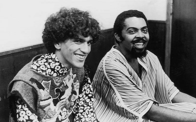 Fotografia histórica em preto e branco dos músicos Caetano Veloso e Gilberto Gil sorrindo, ídolos de inspiração para o preparador vocal Wagner Barbosa.