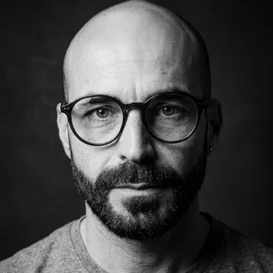 Retrato em close em preto e branco do preparador vocal Wagner Barbosa usando óculos e olhando para a câmera.